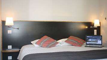 Una cama bien hecha con almohadas a rayas, una computadora portátil sobre la cama y lámparas de noche.