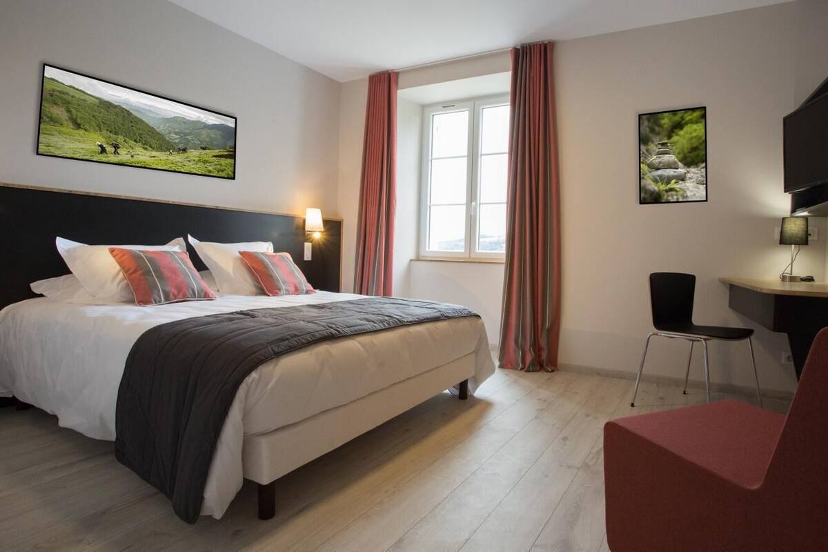 Une chambre d’hôtel avec un lit, un bureau, une chaise, une télévision et deux tableaux accrochés aux murs.