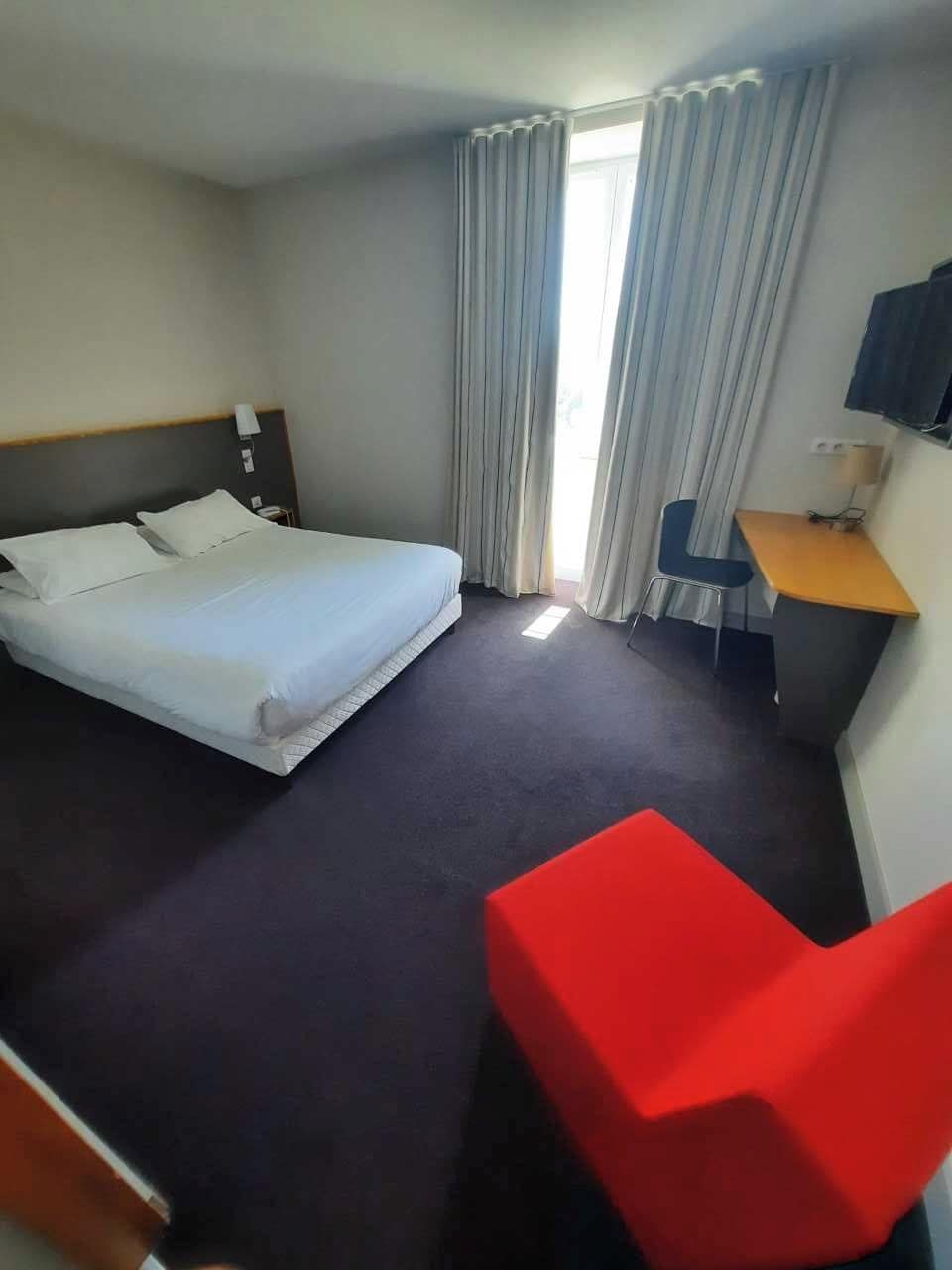 A hotel room with a bed, a desk, a chair, and a window with curtains.