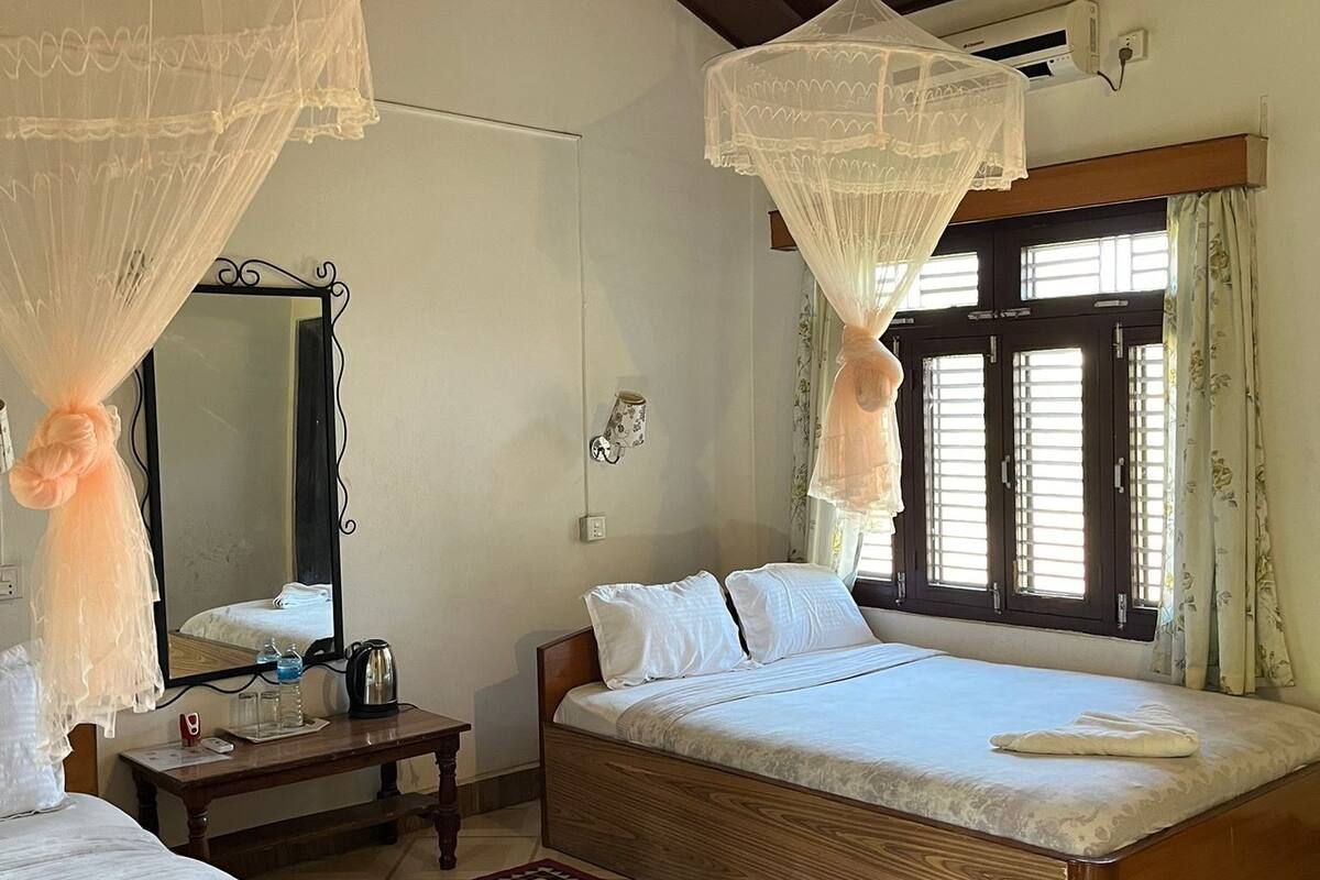 A hotel room with two beds, a wooden headboard, a large mirror, a ceiling fan, and a window with curtains.