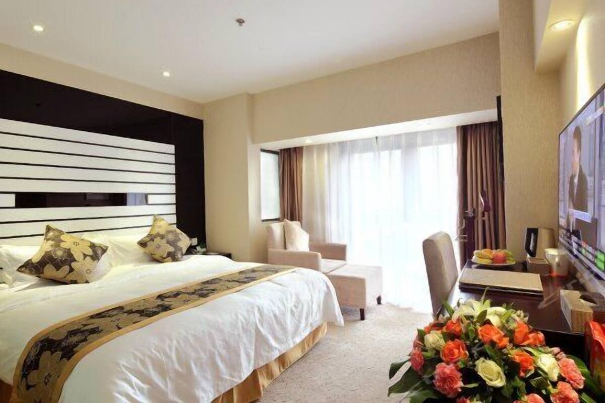 A hotel room with a large bed, a desk with a computer, a TV, and a window with curtains.