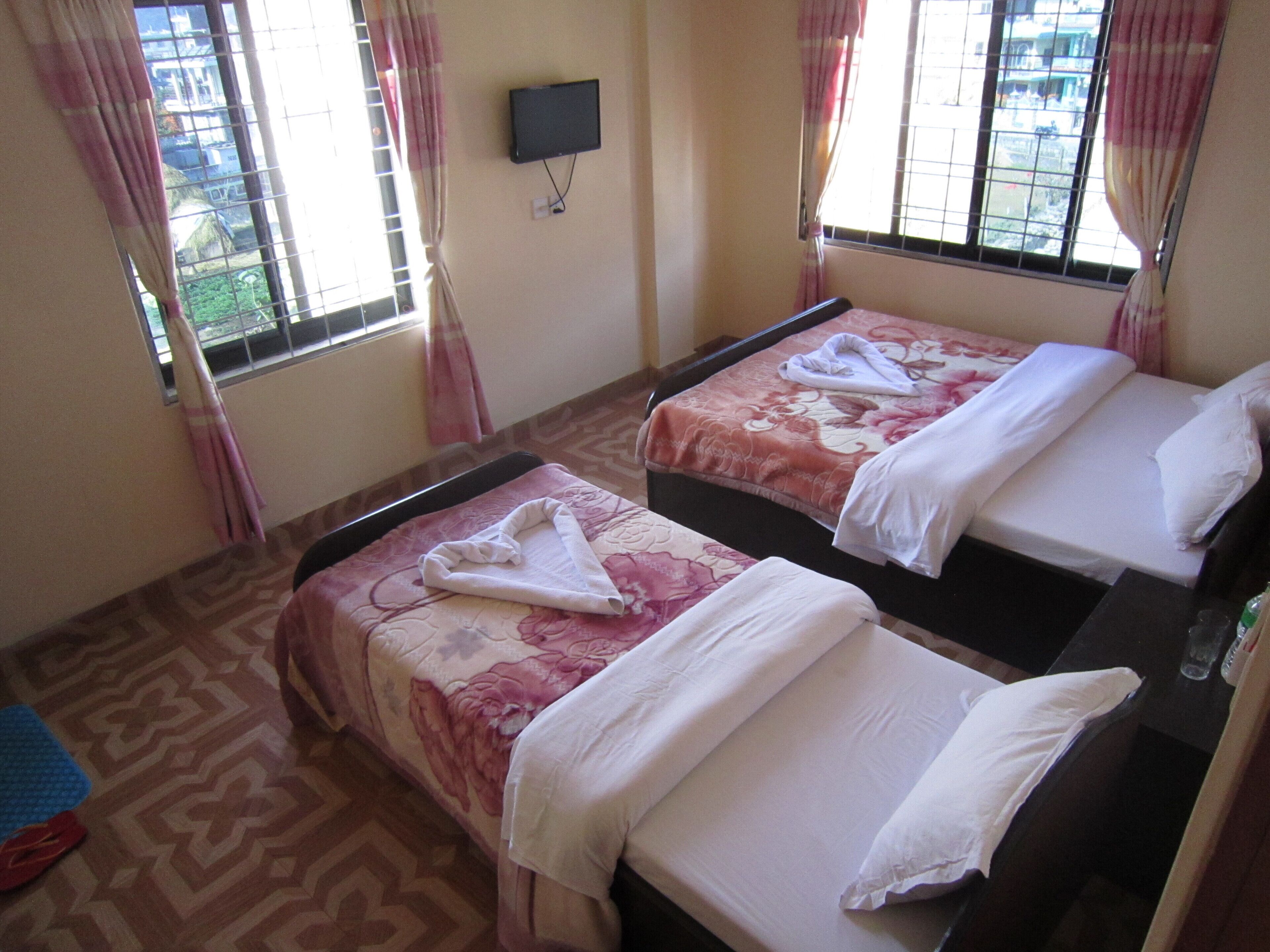 Two single beds with floral bedding, a flat-screen TV on the wall, and a window with curtains.