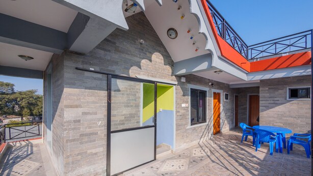 Un edificio moderno con fachada de ladrillo, puerta de vidrio y un balcón con sillas azules.