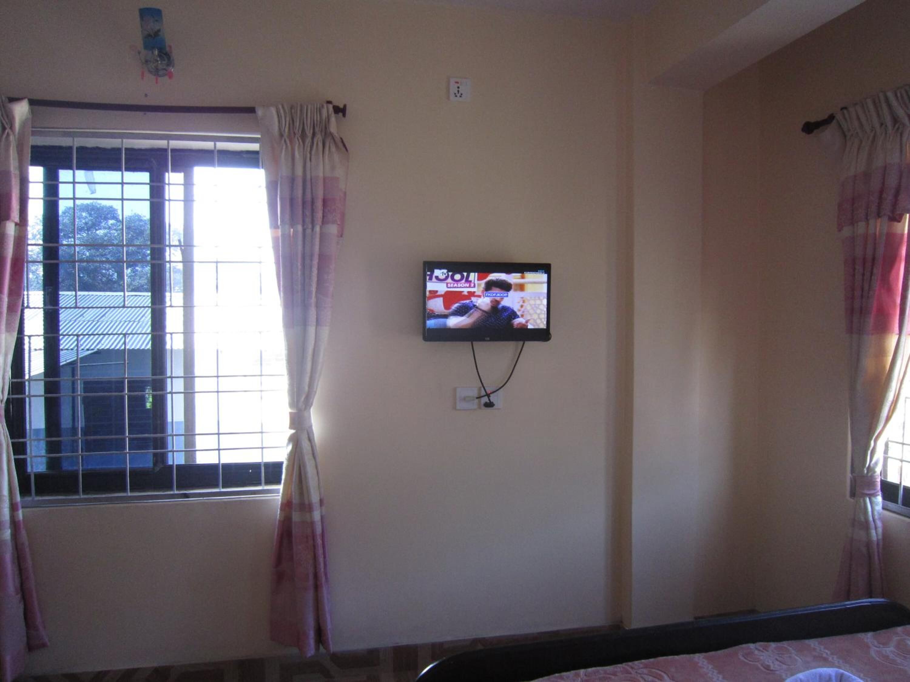 A bedroom with a bed, a TV mounted on the wall, and a window with curtains.