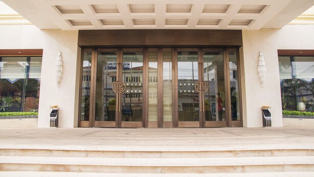 A building entrance with a modern design, featuring a large glass door with a bronze frame, a geometric ceiling pattern, and a small planter on the steps. - Grand Szechuan Hotel Vientiane (Vientiane)
