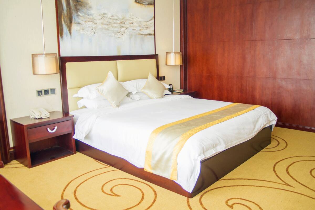 A hotel room with a large bed, two bedside lamps, a nightstand with a phone, and a painting on the wall.