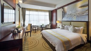 A hotel room with a large bed, a desk, chairs, a small table, and a painting on the wall. - Grand Szechuan Hotel Vientiane (Vientiane)