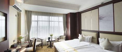 Una habitación de hotel con una cama grande, un escritorio con una silla, una mesita con una lámpara y una ventana con cortinas.