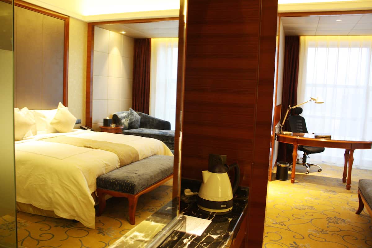 A hotel room with a bed, a desk, a chair, a coffee maker, and a mirror.