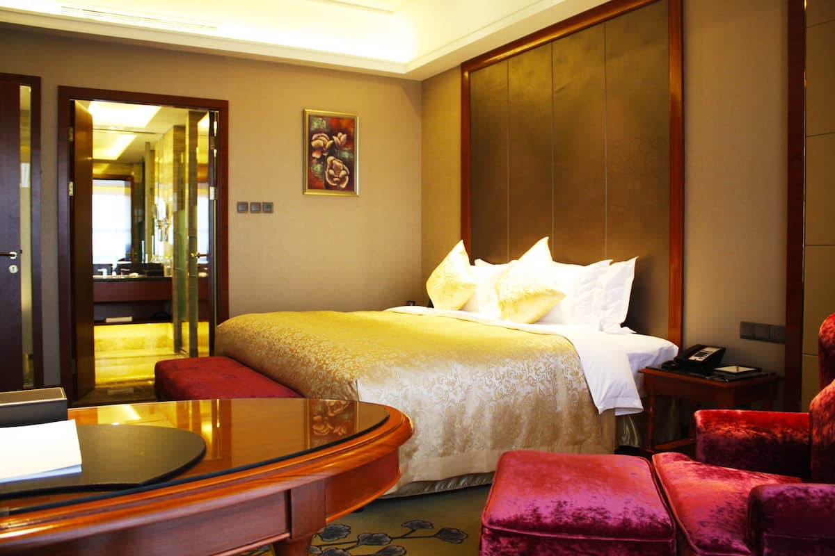 A hotel room with a bed, a desk, a chair, and a bedside table.