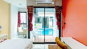 A hotel room with a bed, a small table, a chair, a sofa, a window with curtains, and a sliding glass door leading to a balcony with a pool. - The Pool Resort (Bangkok)