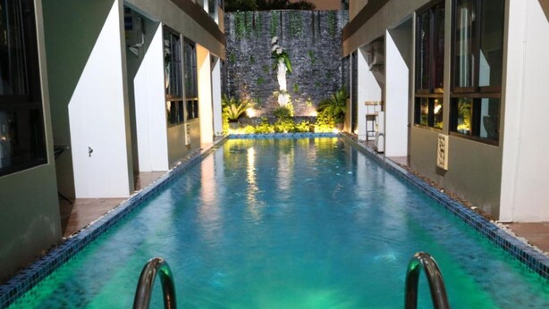 A swimming pool with clear water, surrounded by white walls and a stone wall with greenery in the background. - The Pool Resort (Bangkok)