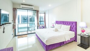 A modern hotel room with a large bed, a balcony with a glass door, and a view of the city. - The Pool Resort (Bangkok)