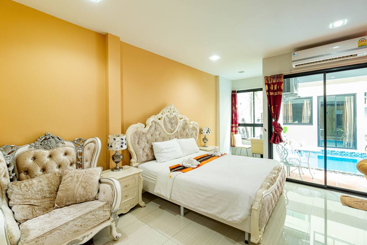 A hotel room with a large bed, a sofa, a nightstand, and a view of a swimming pool.