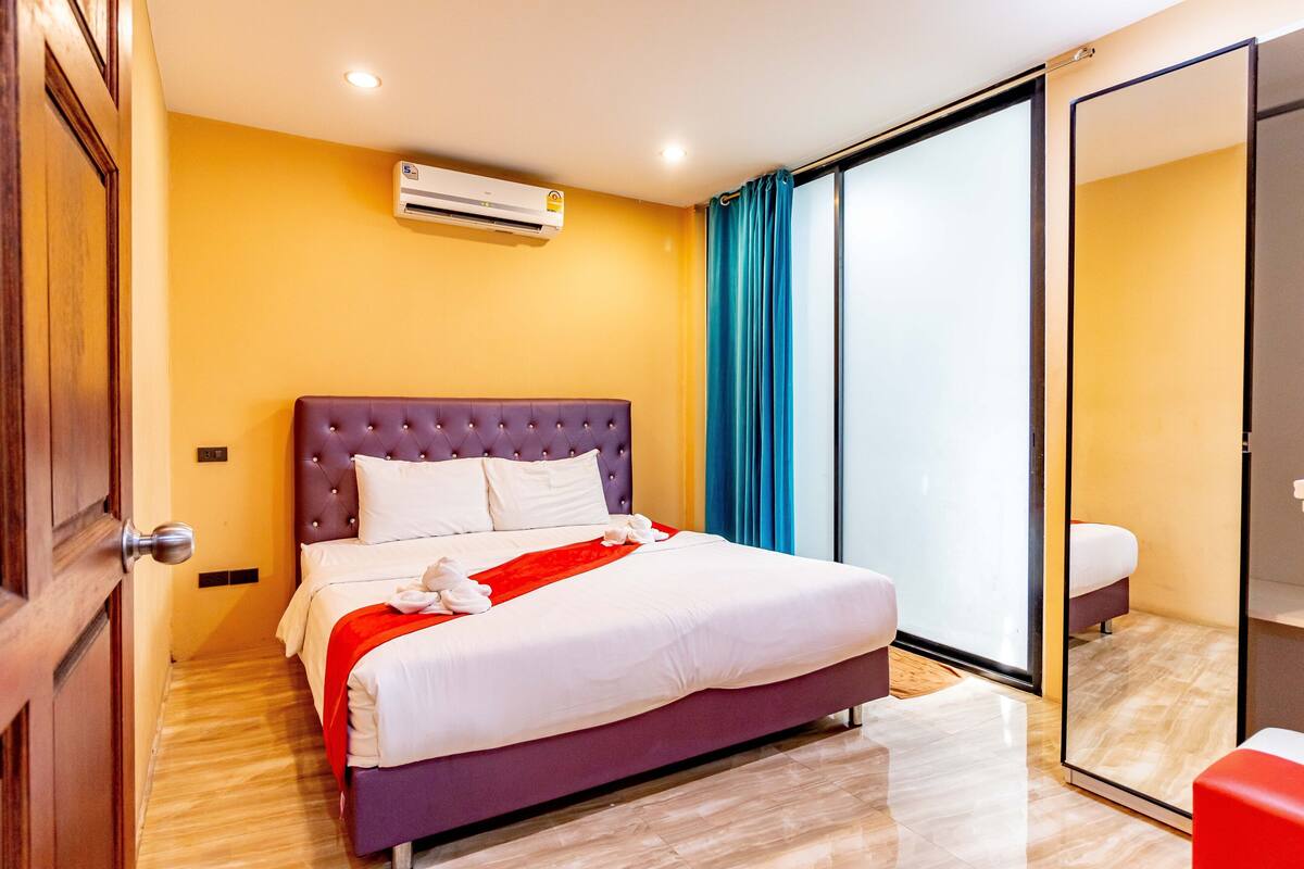 A hotel room with a bed, a sliding glass door, and an air conditioning unit.