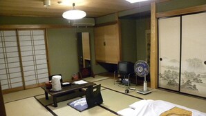 A traditional Japanese room with tatami flooring, a futon bed, a television, a fan, and a shoji screen. - Horieya Ryokan (Fukushima)