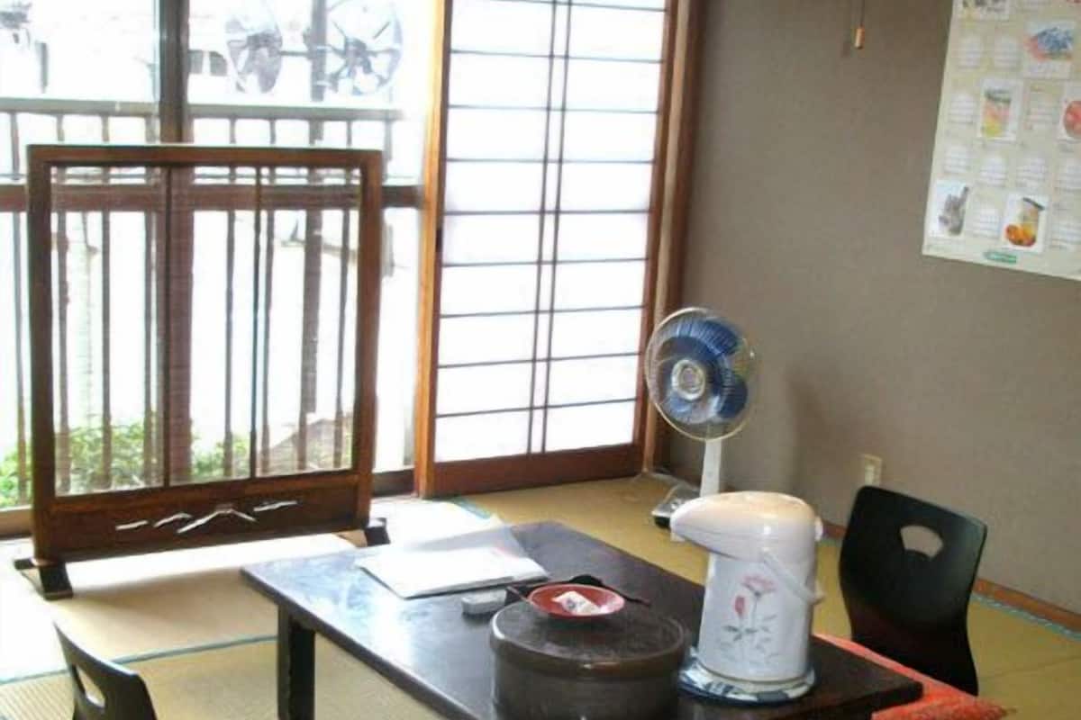 A traditional Japanese room with tatami flooring, a low table, a fan, and a tea set.