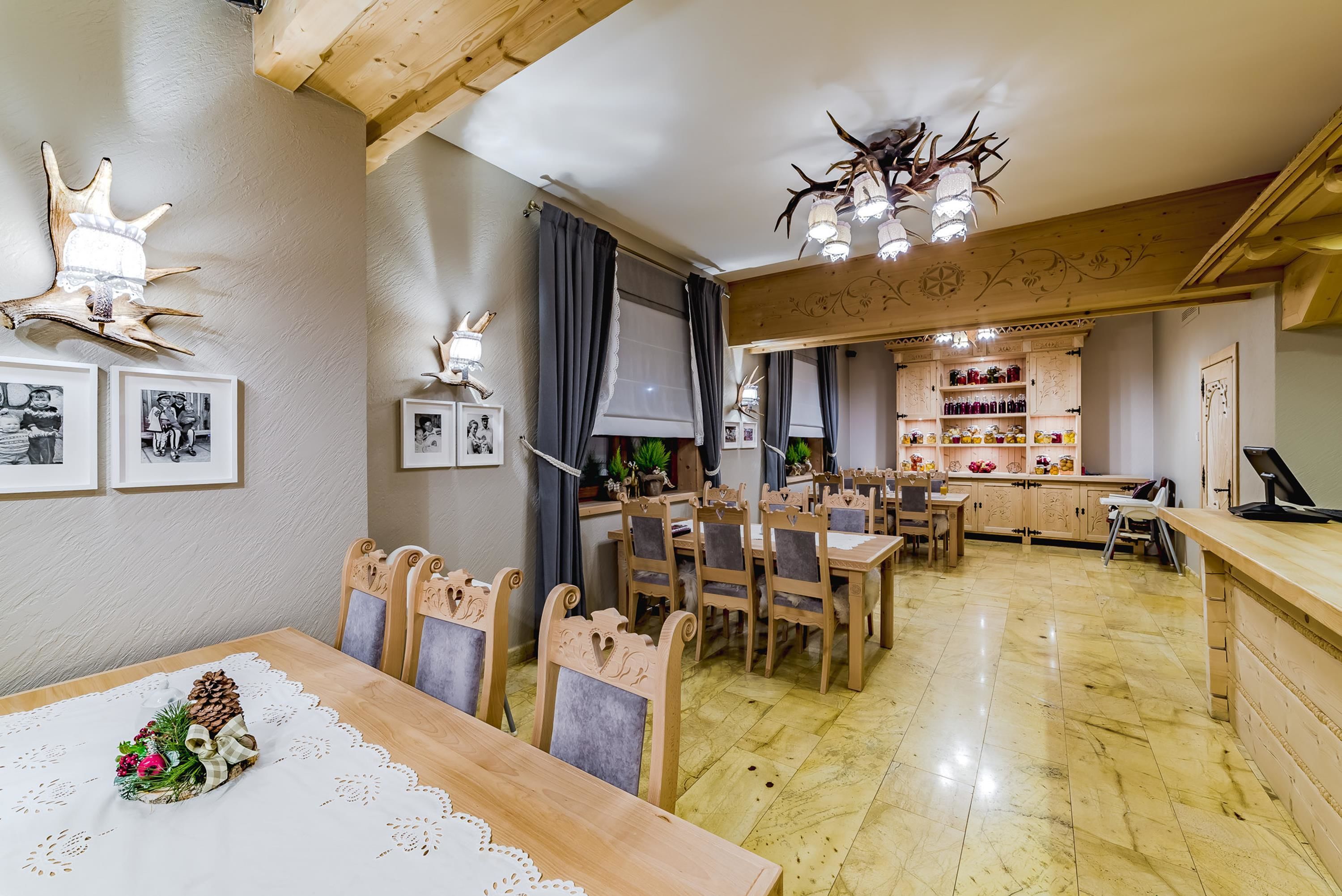 A dining area with wooden tables and chairs, a kitchen in the background, and wall-mounted animal antlers as decor.
