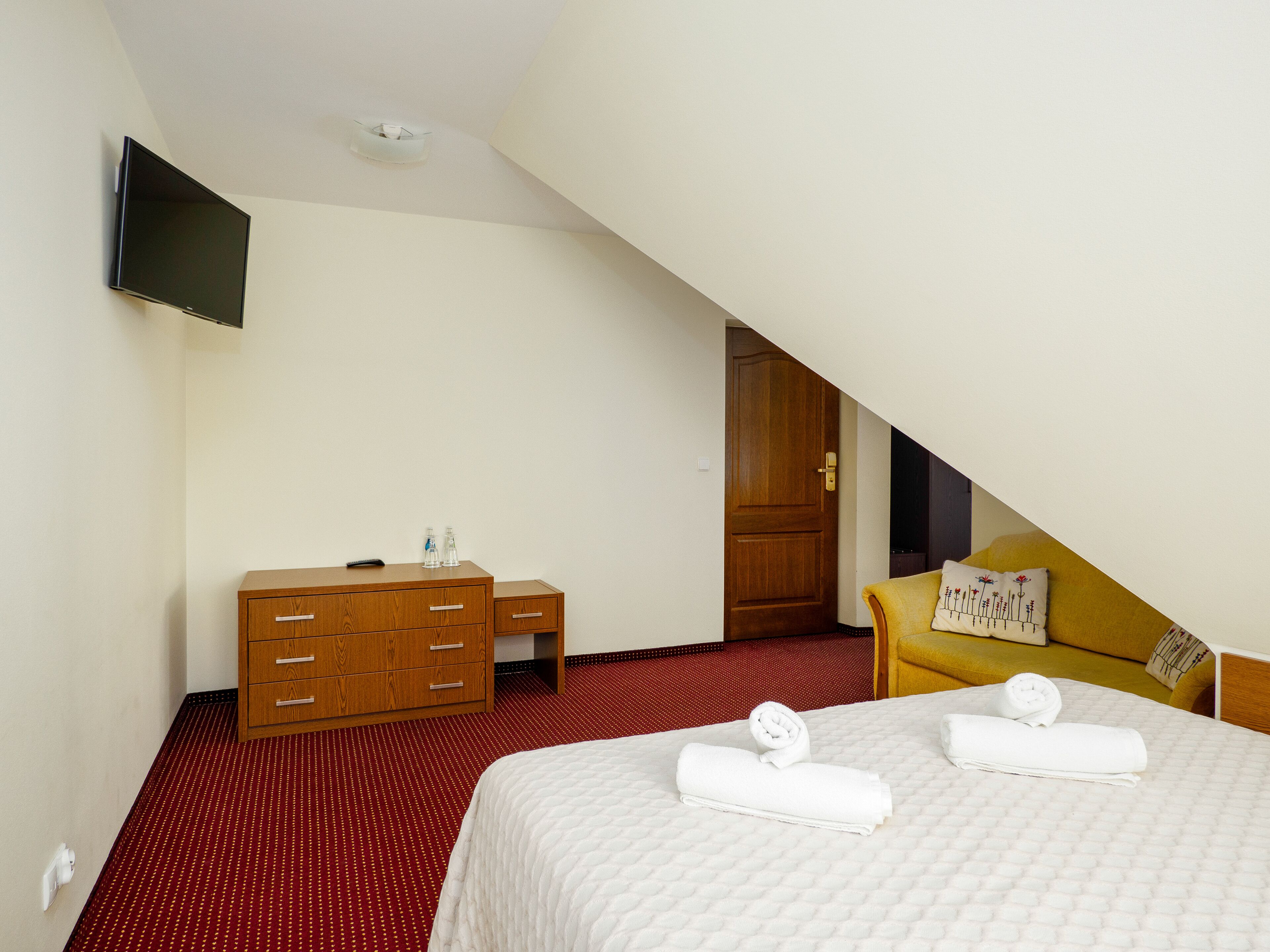 A hotel room with a bed, a wooden dresser, a television, and a door leading to another room.