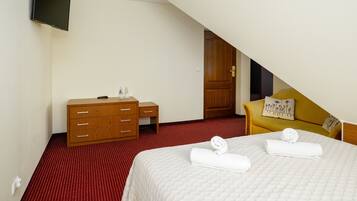 A hotel room with a bed, a wooden dresser, a television, and a door leading to another room.