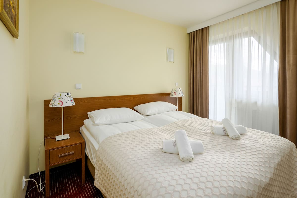 Habitación de hotel con una cama grande, dos lámparas de noche, una mesita de noche de madera y una ventana con cortinas.