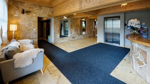 A lobby with stone walls, a wooden ceiling, a reception desk, a sofa with fluffy pillows, and a blue carpet.