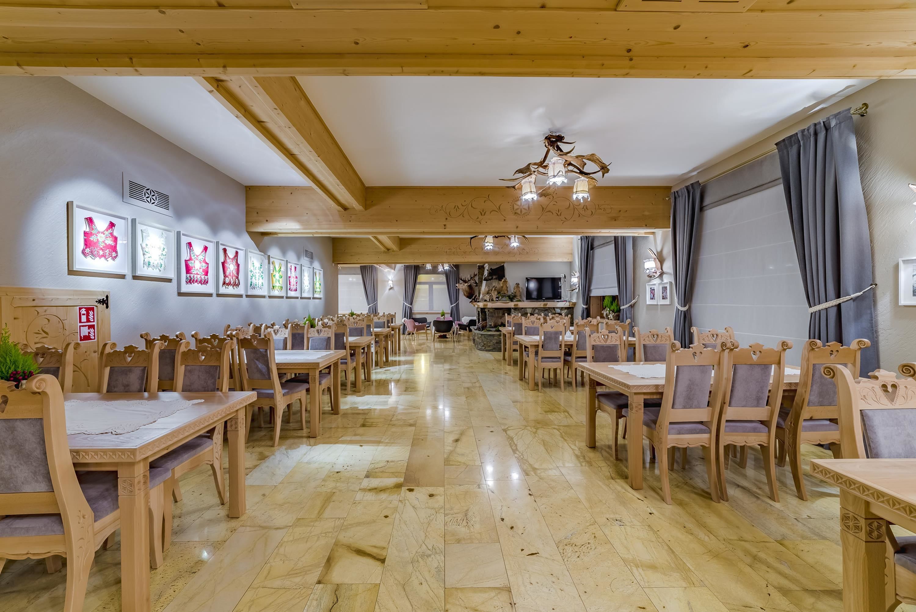 Un comedor con mesas y sillas de madera, una araña y obras de arte enmarcadas en las paredes.