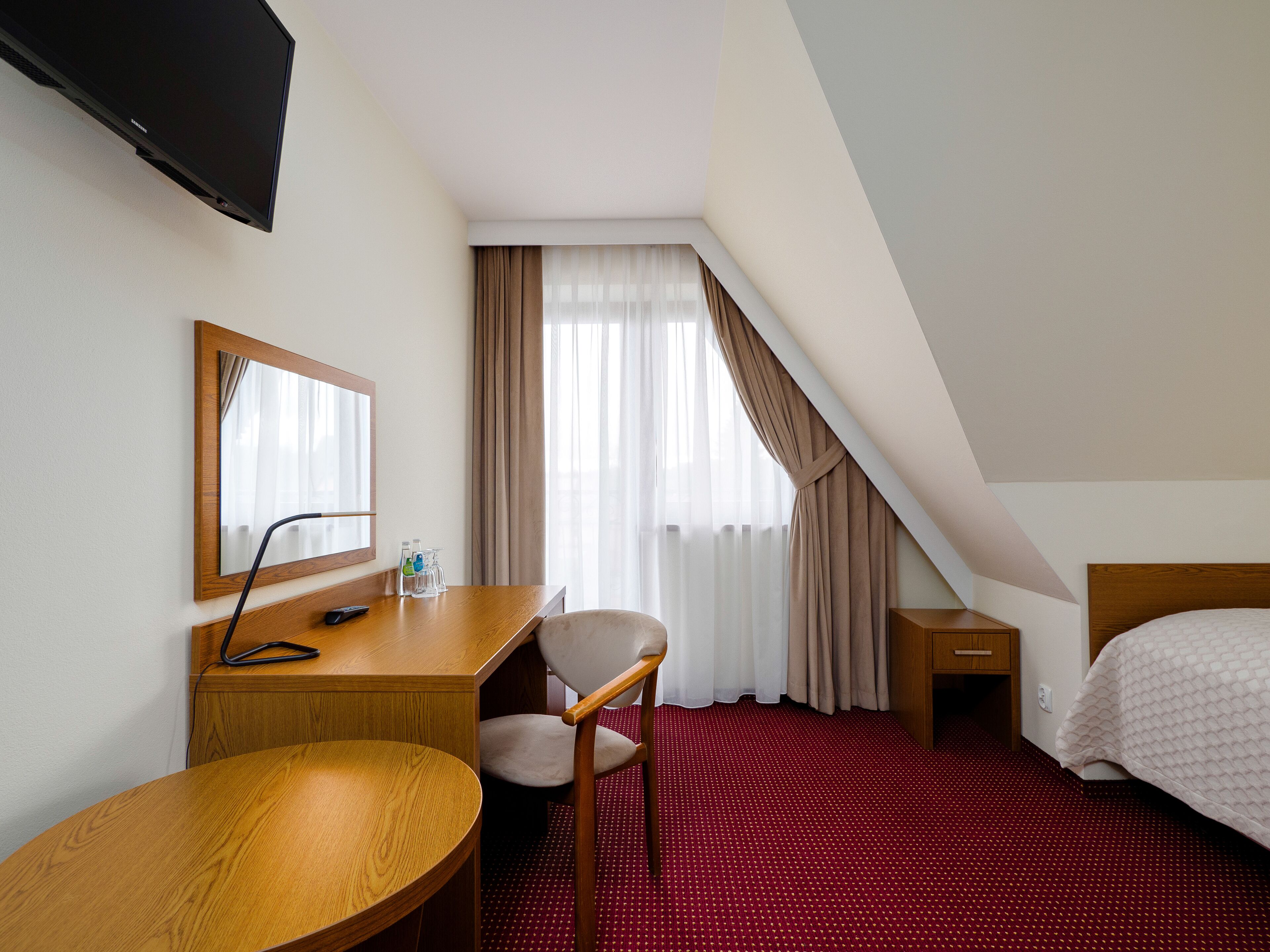 Ein Hotelzimmer mit einem hölzernen Schreibtisch, einem Stuhl und einem Bett mit weißer Daunendecke.