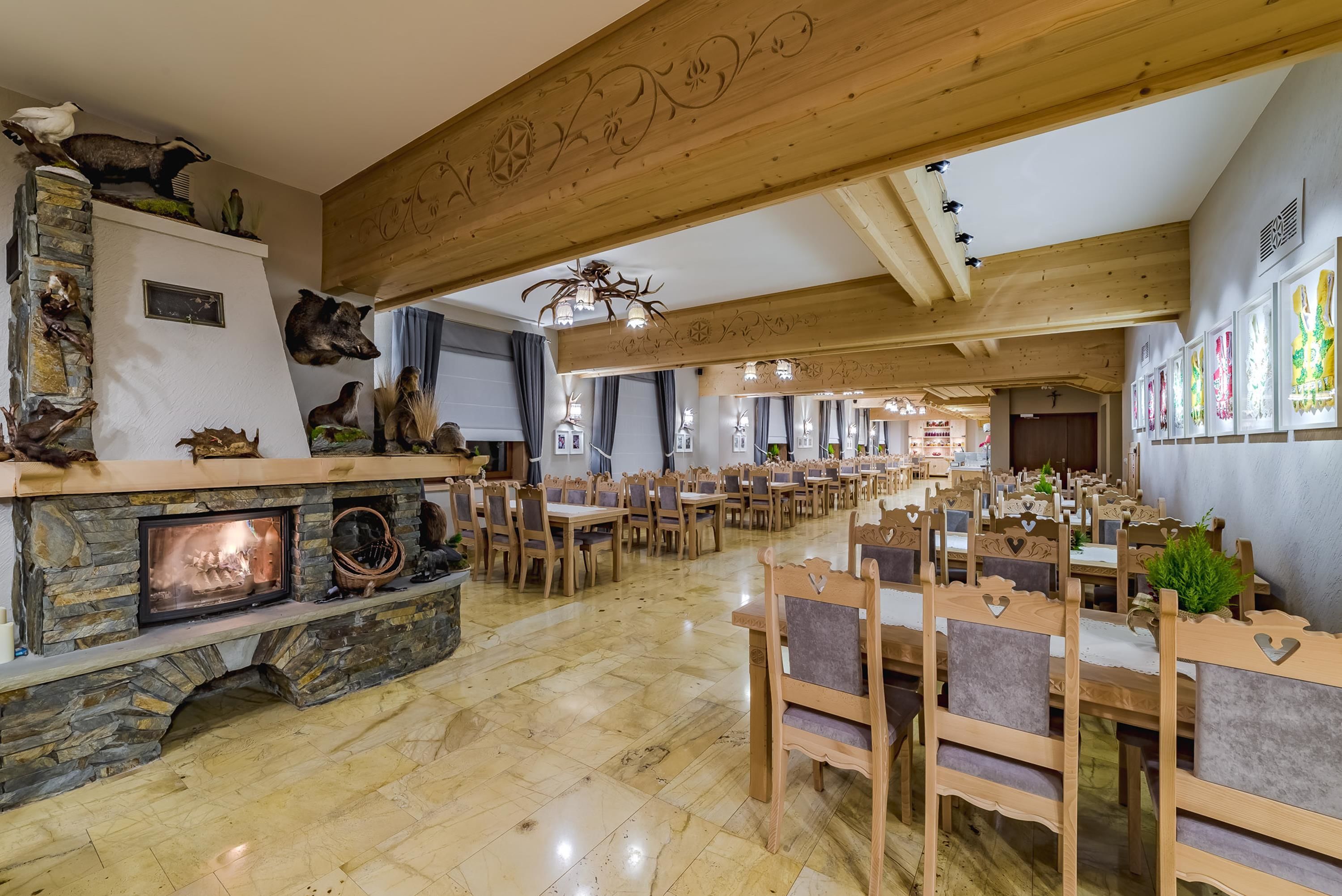 Une salle à manger spacieuse, dotée de tables et de chaises en bois, d’une cheminée en pierre et de diverses décorations représentant des animaux et des plantes.