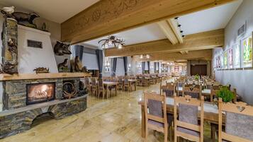 Un amplio comedor con mesas y sillas de madera, una chimenea de piedra y diversas decoraciones de motivos animales y vegetales.