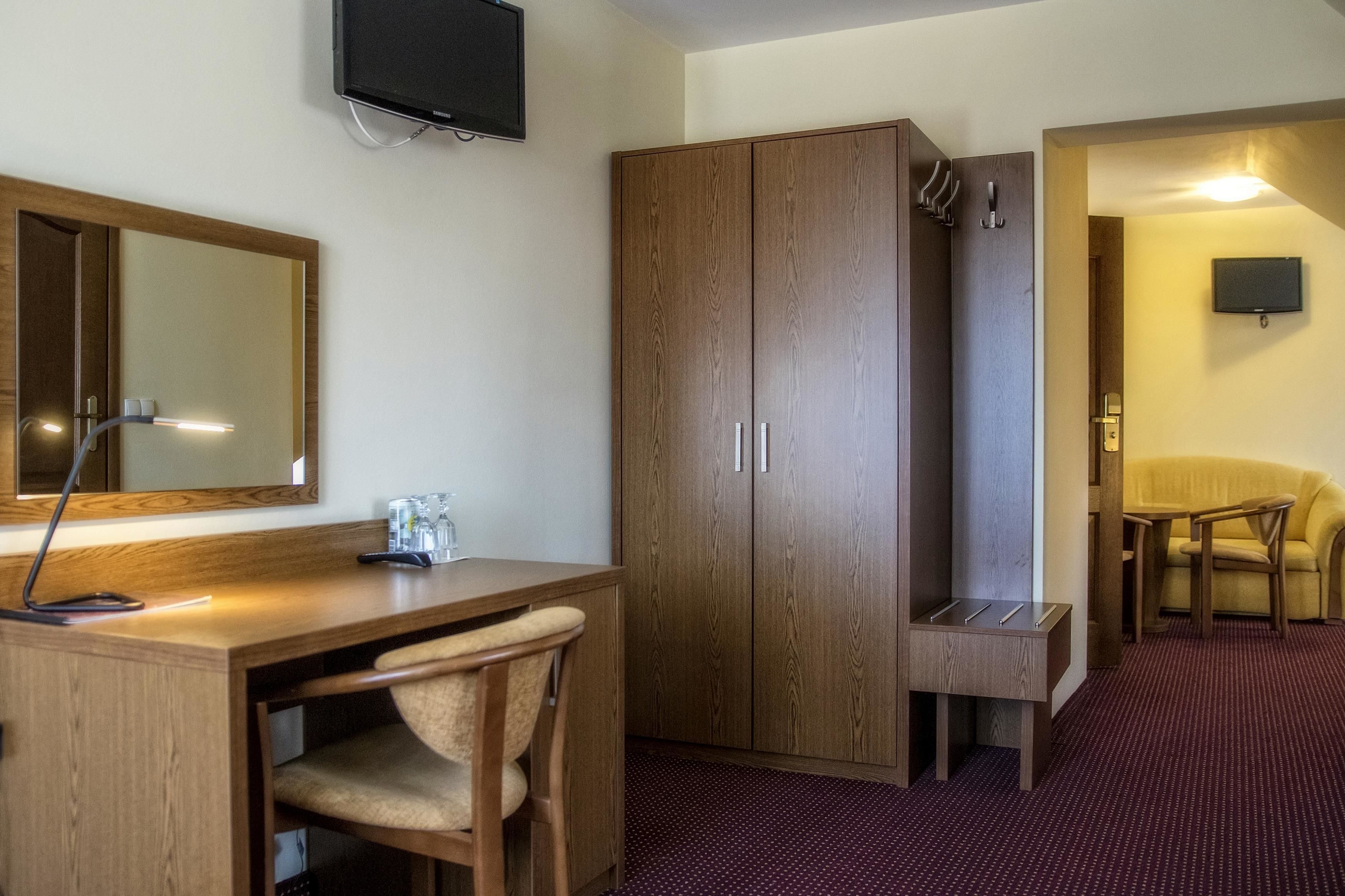 Une chambre d’hôtel avec un bureau en bois, un miroir, une armoire, une petite table, une chaise et un téléviseur fixé au mur.
