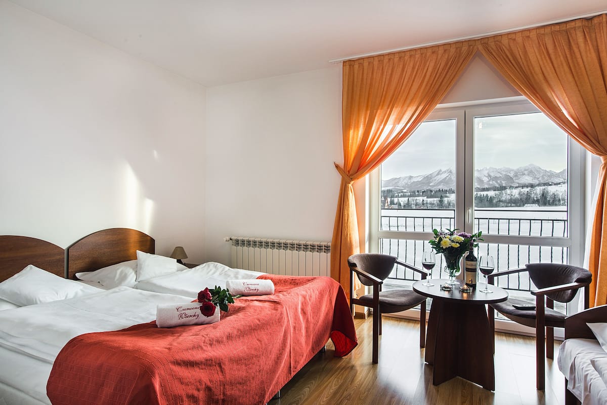 Ein Hotelzimmer mit Bett, Tisch mit Stühlen und Bergblick durch das Fenster.