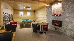 Een gezellige ruimte met een pooltafel, comfortabele zitplaatsen, een open haard en een stenen muur.