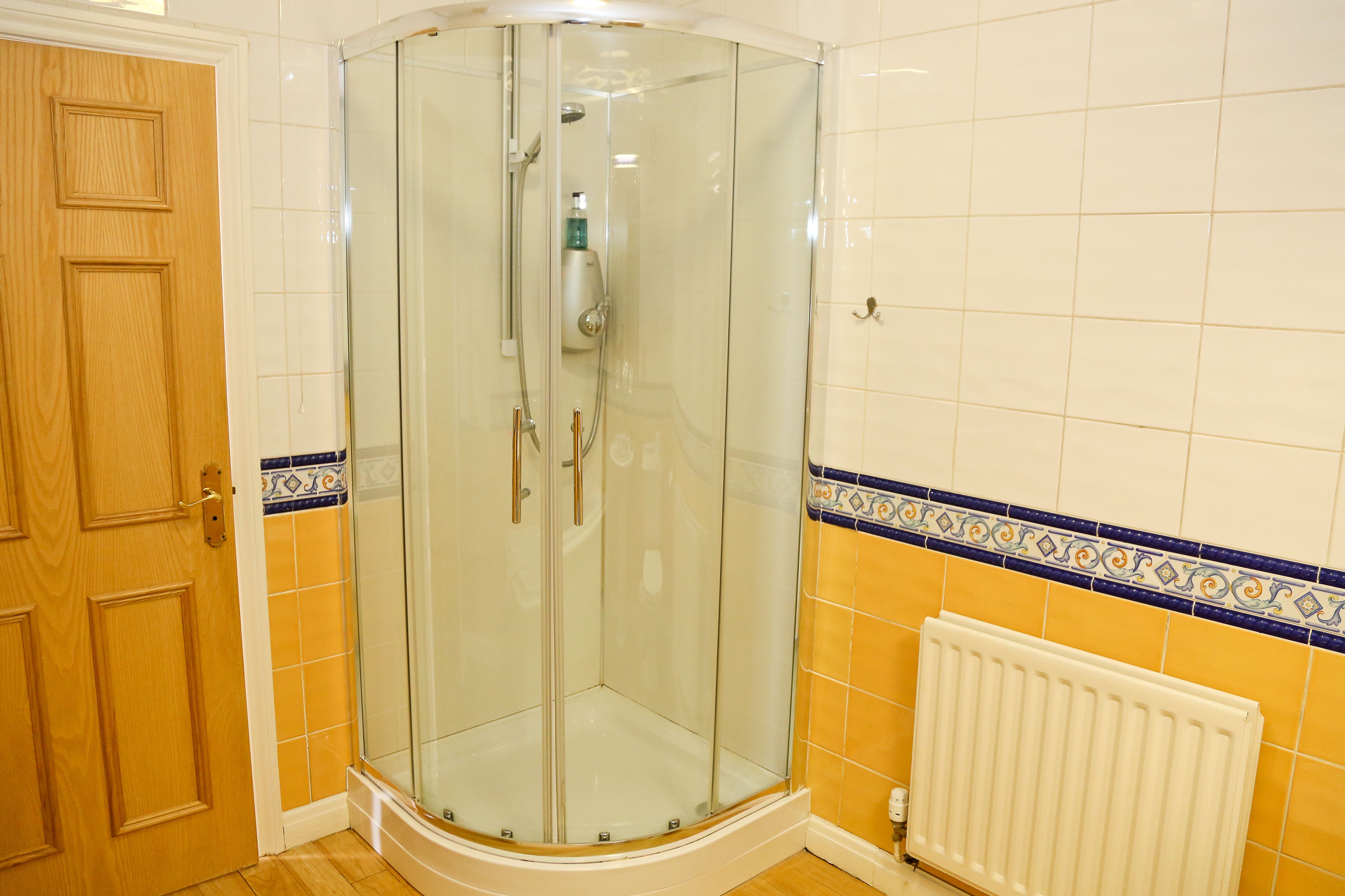 Een douche in een hoek met glazen deuren, een houten deur en een betegelde muur met decoratieve rand.