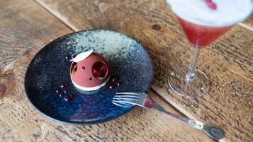 Un postre sobre un plato azul, con un tenedor al lado y una copa de martini con una cereza en el borde.