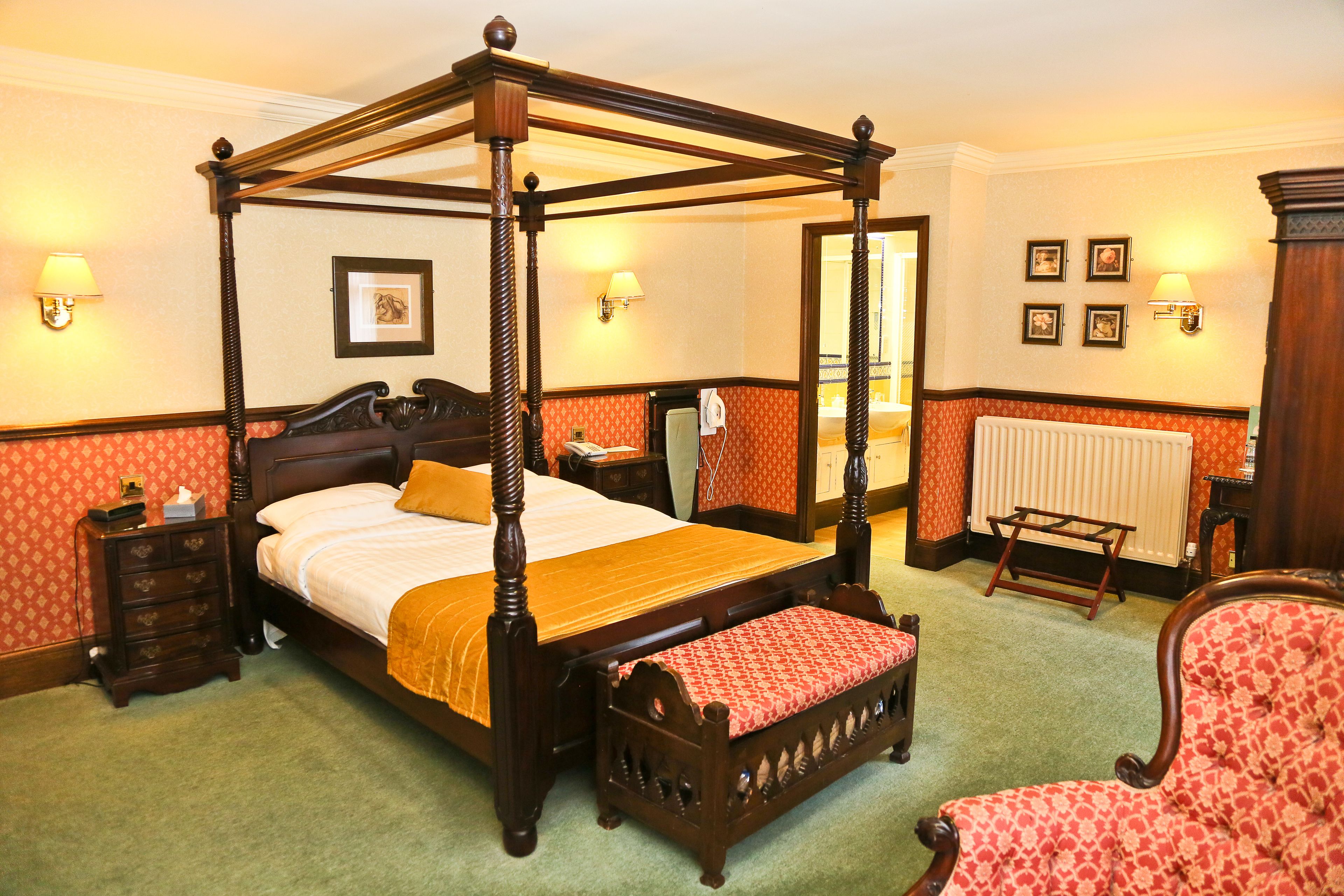 A four-poster bed with a wooden frame, a nightstand with a lamp, and a red patterned chair.