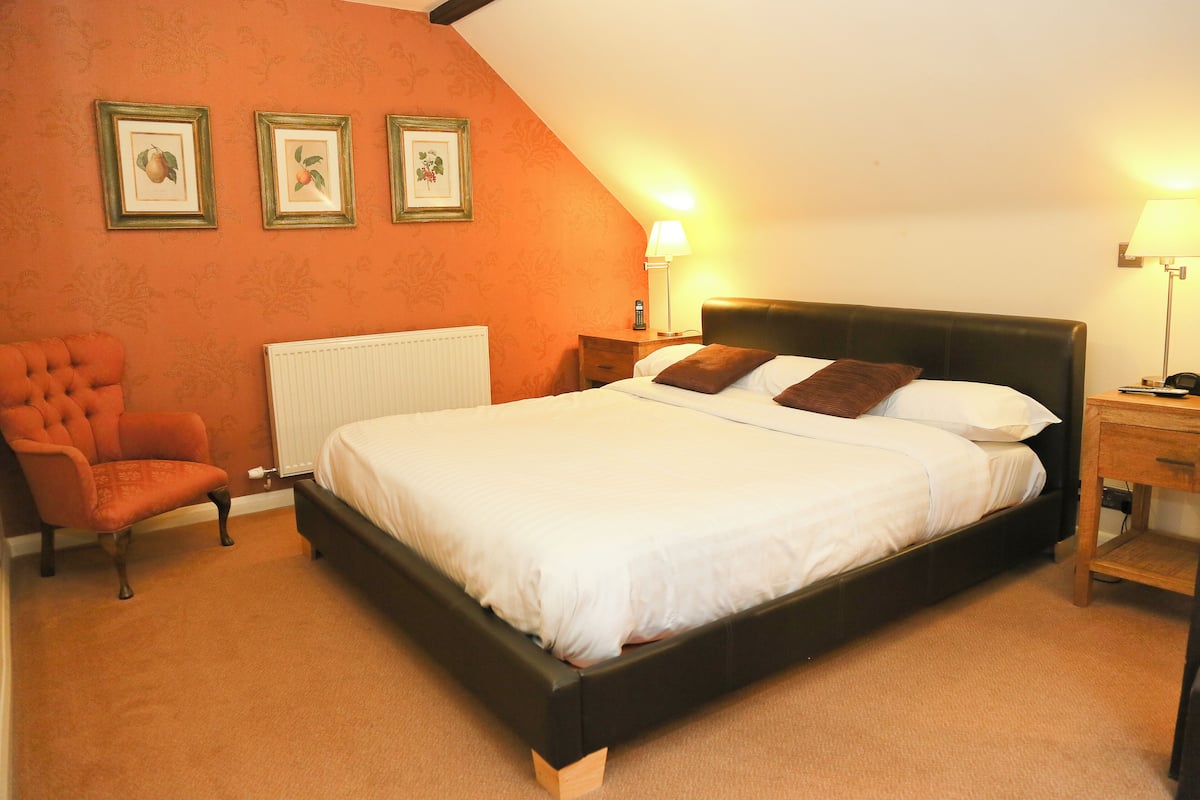 A bedroom with a large bed, a chair, and three framed pictures on the wall.