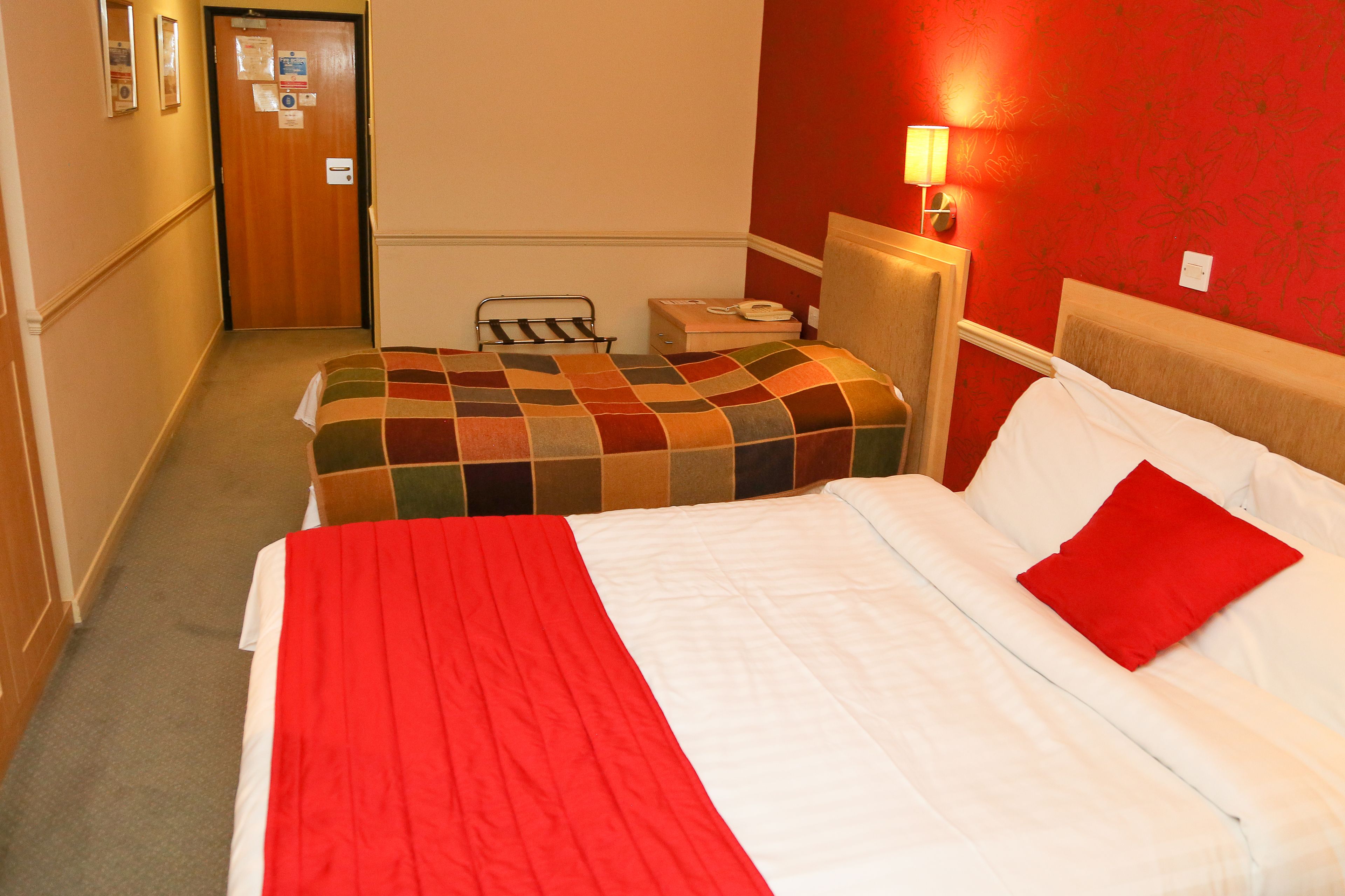 A hotel room with two beds, a wooden headboard, a nightstand with a lamp, and a door with a mirror and a sign.