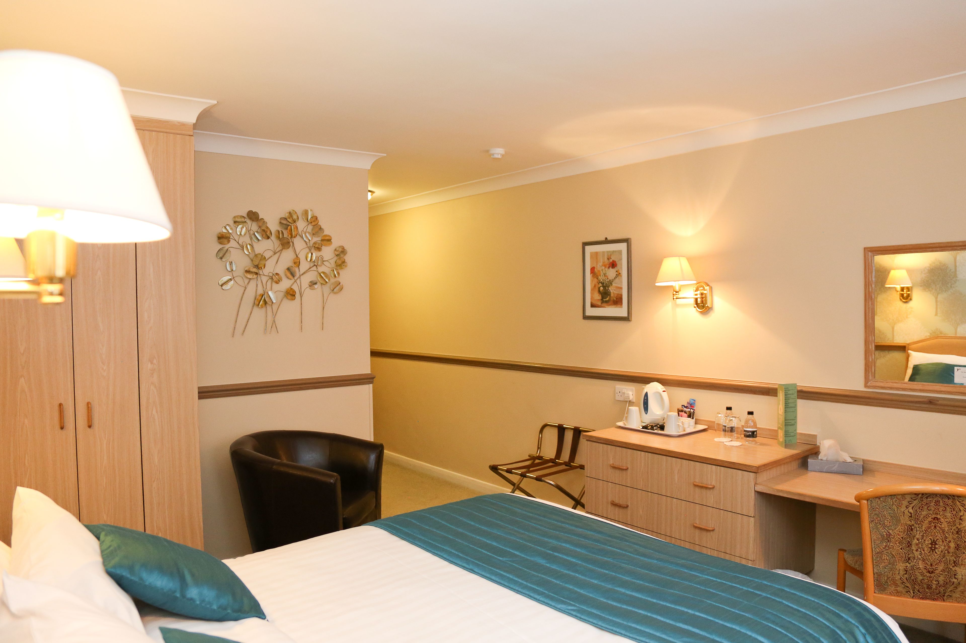 Una habitación de hotel con cama, escritorio, silla, armario y lámparas fijadas a la pared.