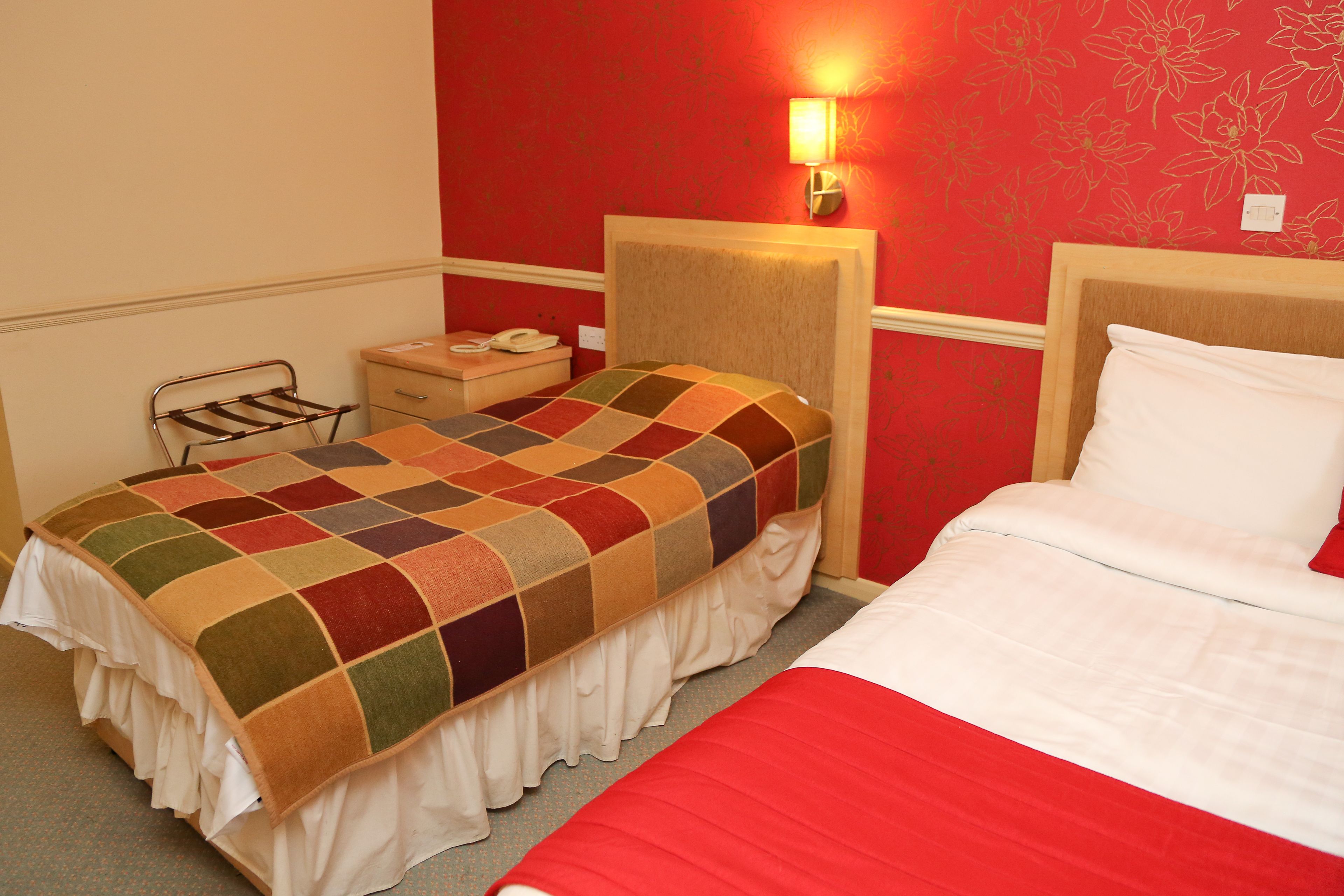 A hotel room with a bed, a bedside table, a lamp, and a wall with floral wallpaper.