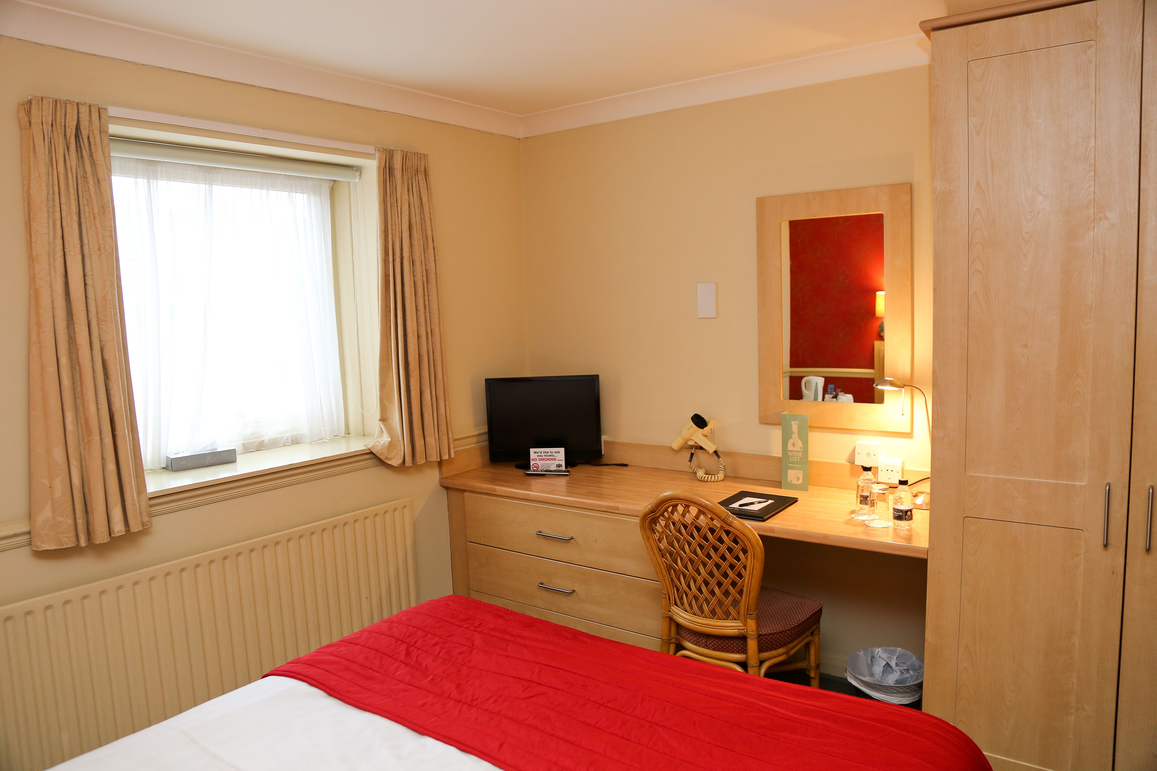 A hotel room with a bed, a desk with a computer, a chair, a mirror, and a wardrobe.