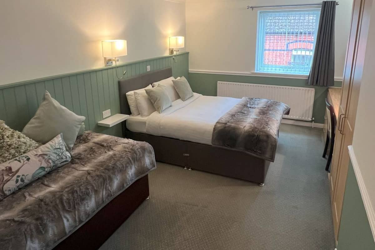 A hotel room with two beds, a small table, and a window with curtains.