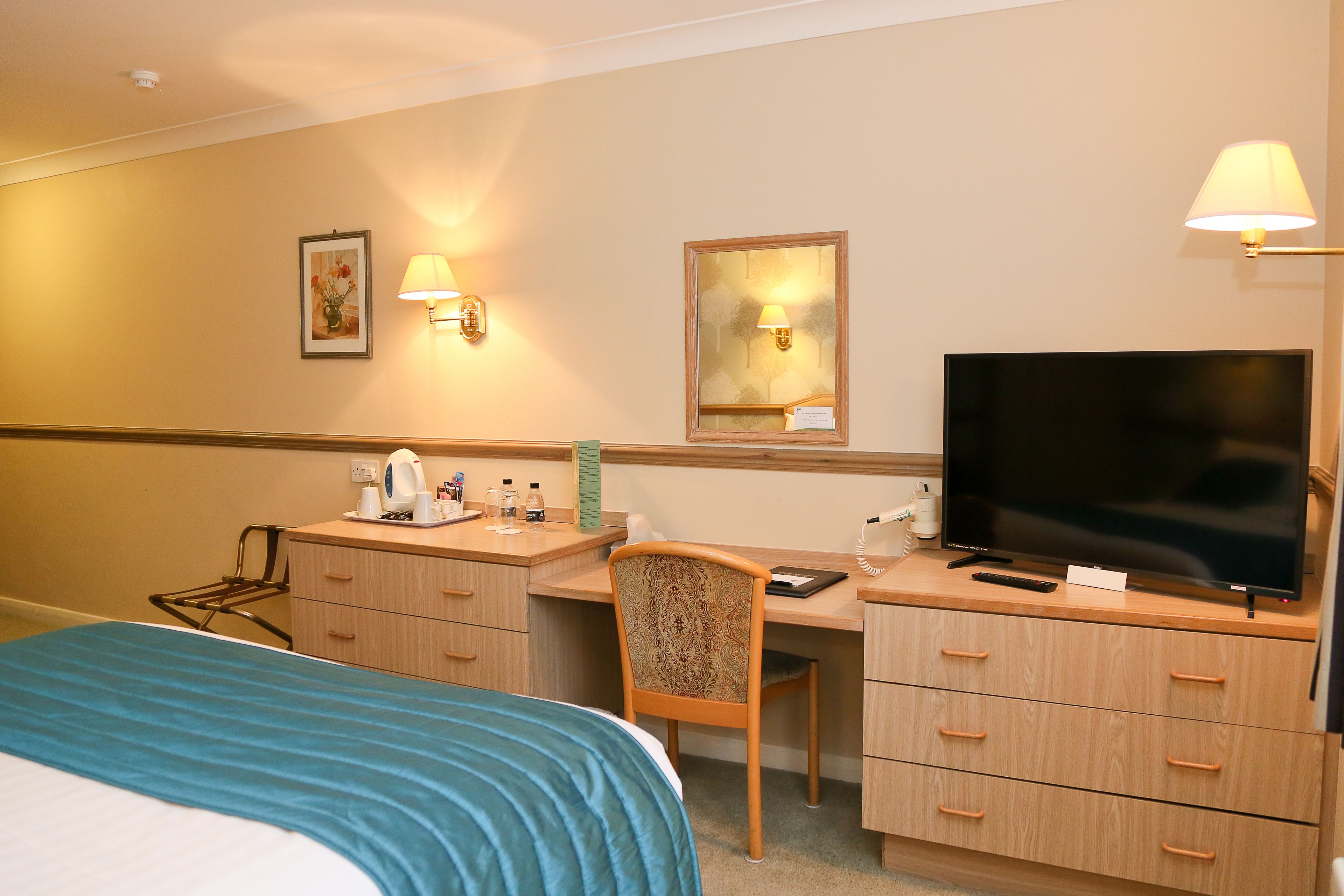 Ein Hotelzimmer mit Bett, Schreibtisch, Stuhl, Fernseher und Wandlampen.