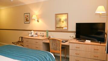 Ein Hotelzimmer mit Bett, Schreibtisch, Stuhl, Fernseher und Wandlampen.