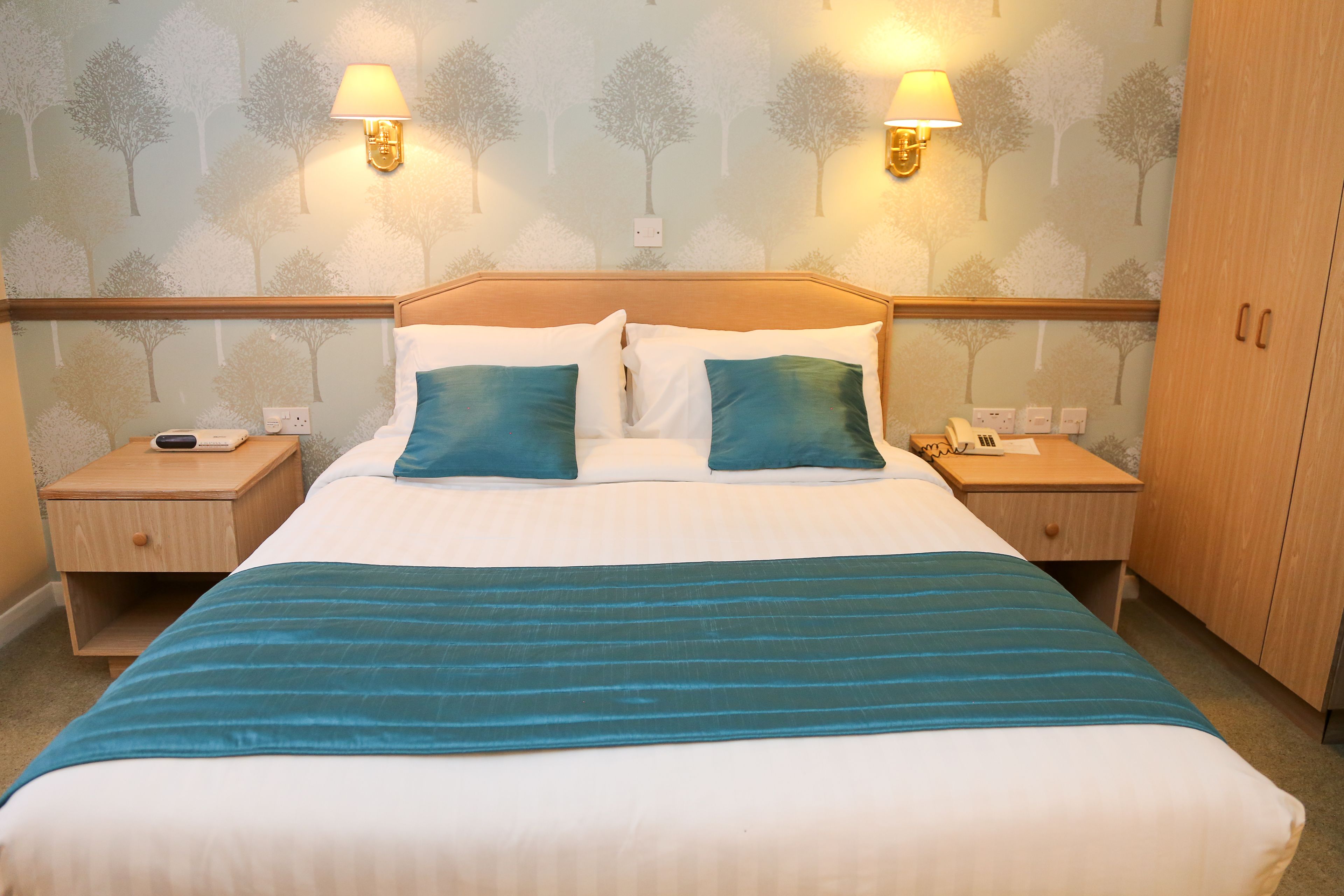 A neatly made bed with a teal-striped bedspread, two matching pillows, and two bedside lamps.