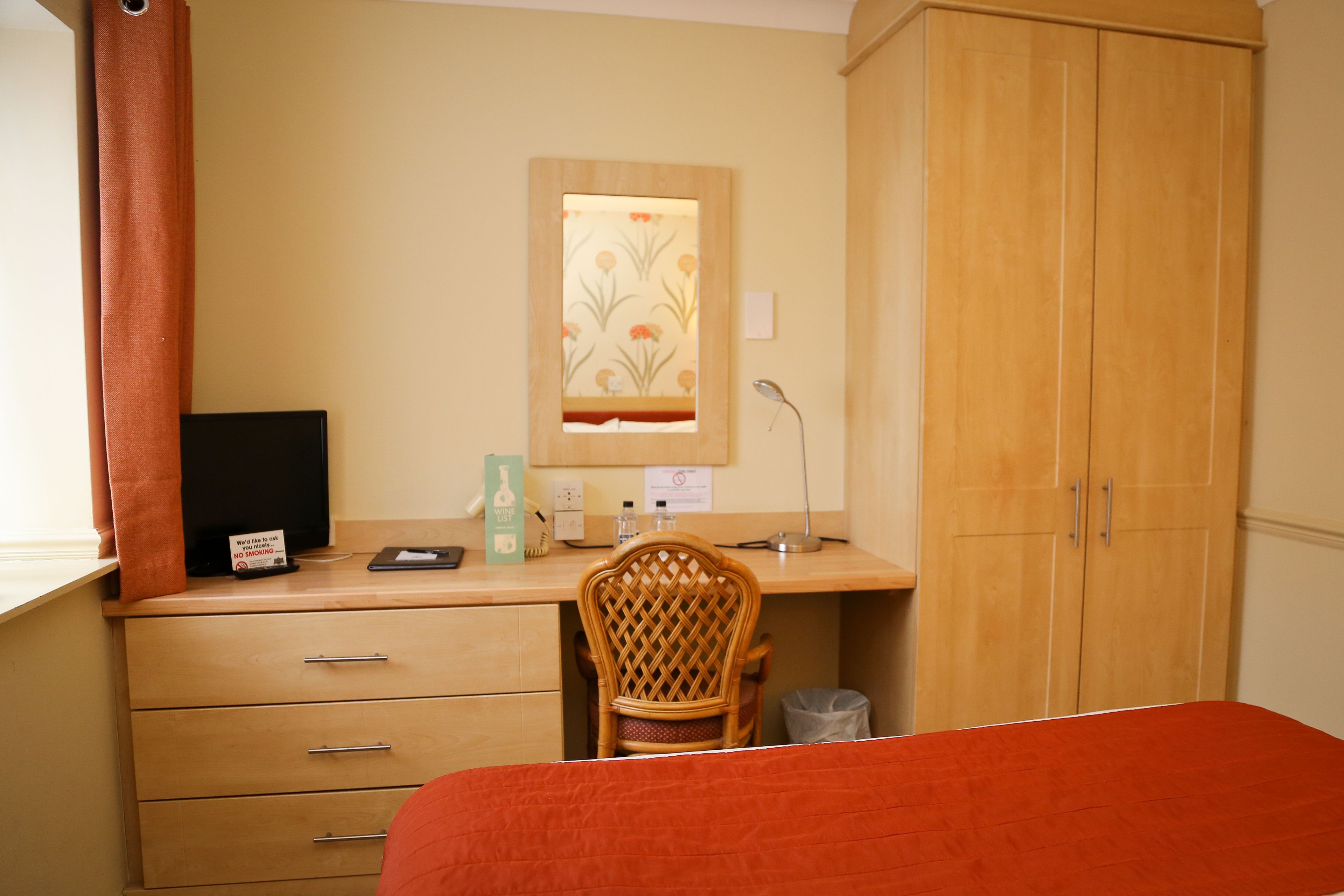 Una habitación con escritorio de madera, una silla, una cama, un armario y una ventana con cortinas.