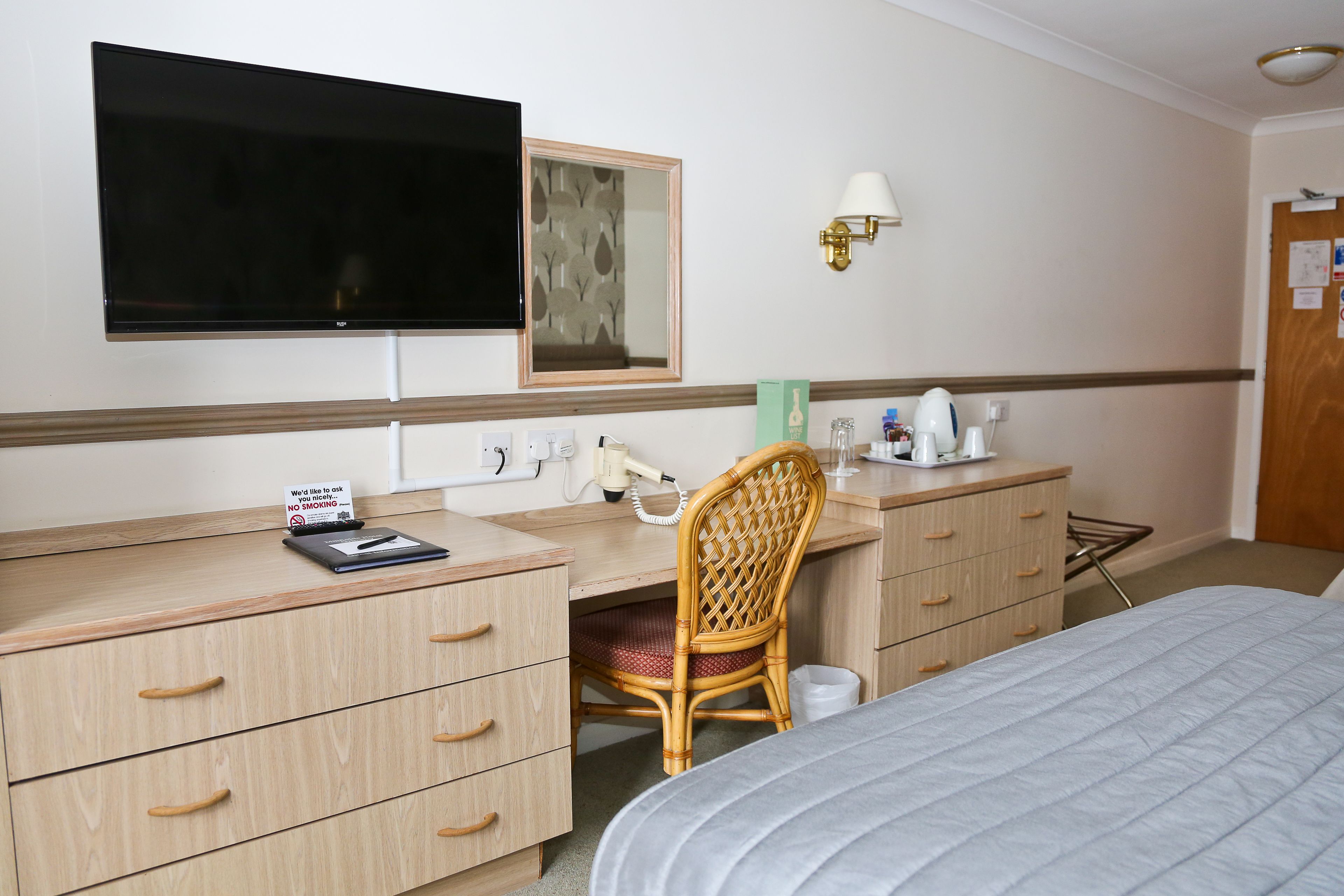 Ein Hotelzimmer mit Bett, Schreibtisch mit Stuhl, Fernseher, Spiegel, Lampe und einem Schild mit Rauchverbot.