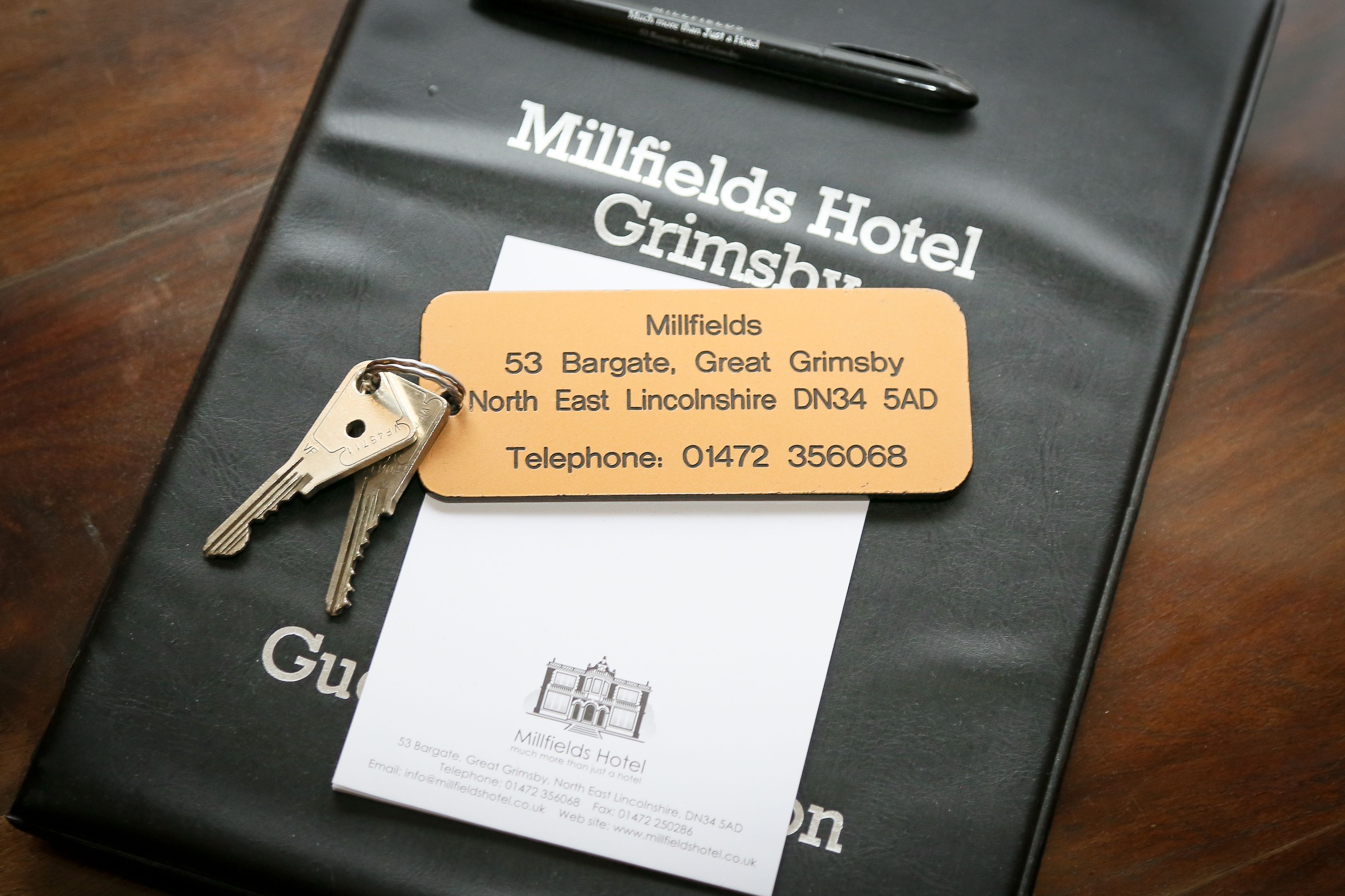 A black Millfields Hotel Grimsby brochure with a business card and keys on top.