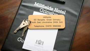 A black Millfields Hotel Grimsby brochure with a business card and keys on top.