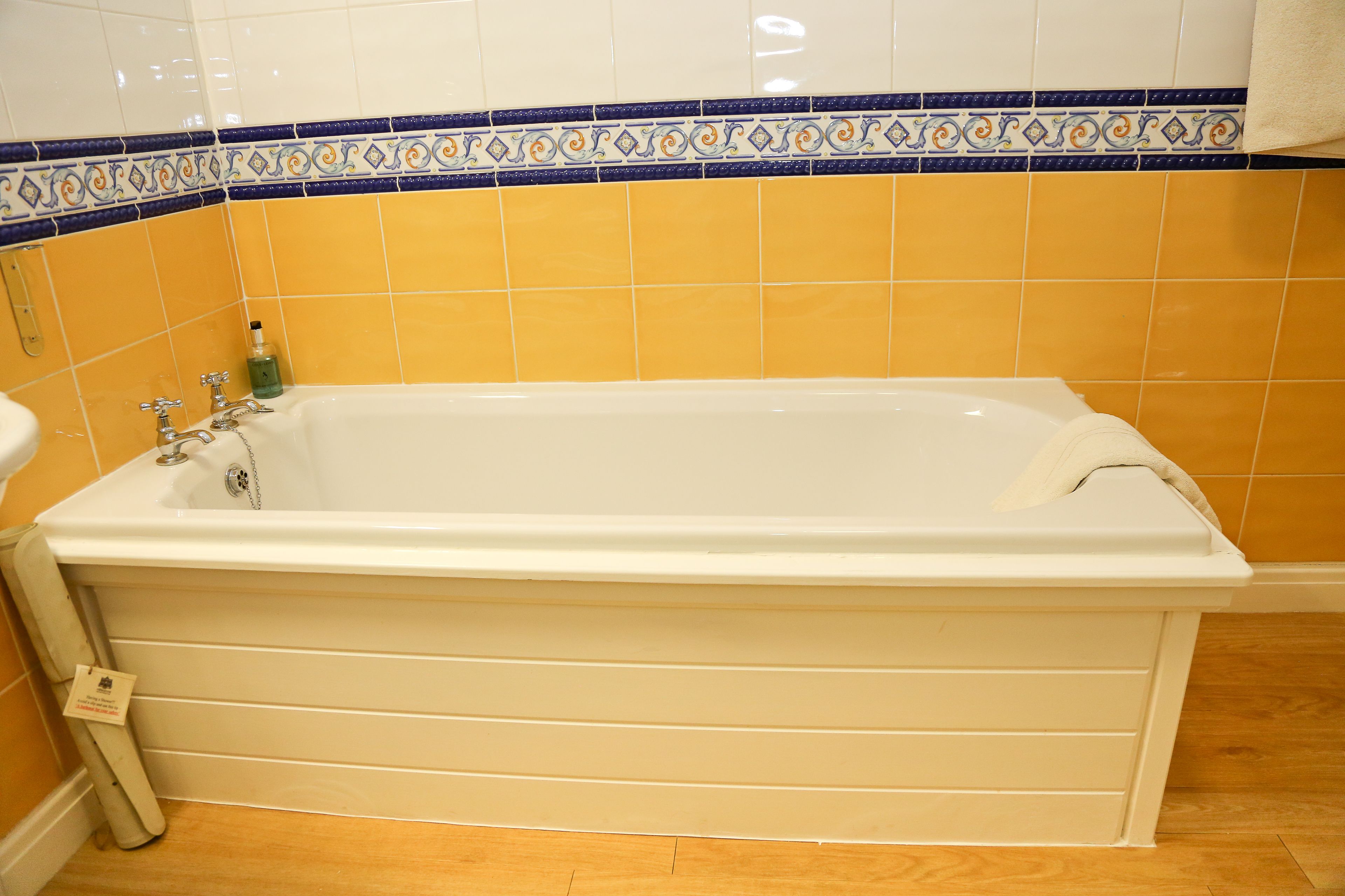 Een badkamer met een bad, gele tegels en een decoratieve rand.